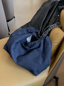 Large denim tote bag with silver chain straps shown on a leather chair in a casual setting