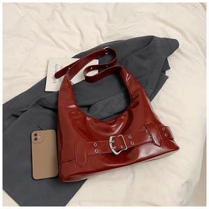 Close-up of bright red patent leather shoulder bag with silver buckle on fabric background