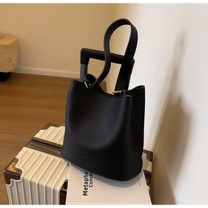 Gros plan du sac seau noir en cuir avec détails dorés sur une valise blanche