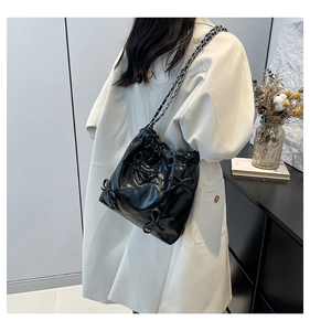 Dettaglio di una borsa a secchiello trapuntata nera con fiocchi e tracolla a catena su modella