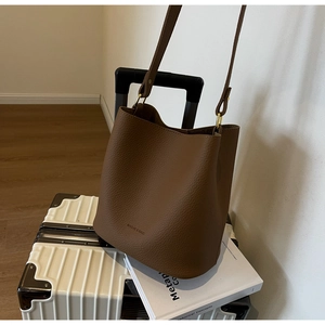 Détail du sac seau en cuir grainé marron foncé avec boucle dorée et logo imprimé