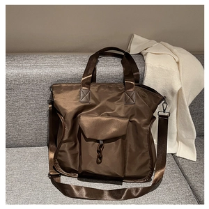 Detailed view of brown nylon tote bag with adjustable strap and chain pocket on sofa