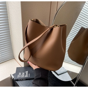 Détail du sac seau en cuir grainé marron avec logo embossé et bandoulière en cuir