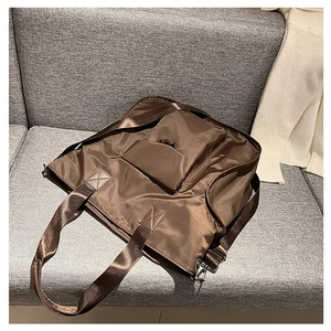 Detail view of large brown nylon tote bag with crossbody strap on a grey sofa background