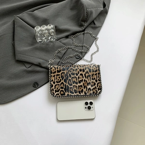 Close-up of leopard print crossbody bag with silver studs and chain next to a smartphone