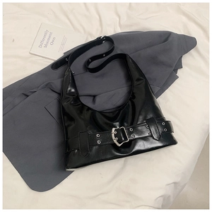 Detail of glossy black faux leather shoulder bag featuring silver buckle and metal eyelets