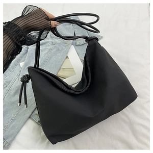 Détail d'un grand sac cabas noir avec nœud décoratif et fines bretelles de transport