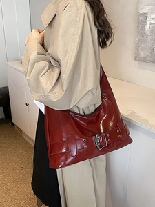 Glossy dark red leather hobo bag with silver buckle worn with a beige trench coat