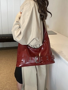 Glossy burgundy patent leather underarm bag with decorative silver buckle on model