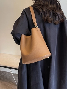 Sac seau en cuir marron avec large bandoulière, porté par un mannequin en manteau noir