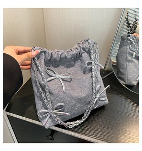 Dettaglio borsa a secchiello in denim grigio con fiocchi in metallo argento e catena