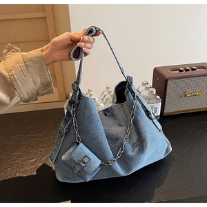 Detail of blue denim tote bag with silver chain and mini charm against retro props