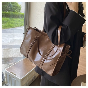 Detail der großen braunen PU-Leder-Tote mit seitlicher Schleife und glänzendem Finish
