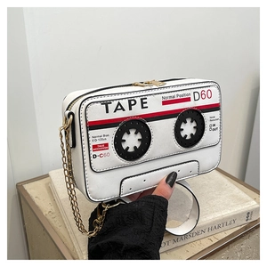 Close-up of retro cassette-shaped white crossbody bag with gold chain strap on books