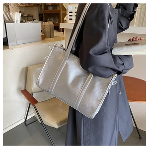 Silberne Metallic-Tote-Tasche mit seitlichen Nieten und Kordelzug-Detail im modernen Stadtcafé