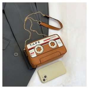 Close-up of retro cassette tape shaped crossbody bag with gold chain on grey blazer