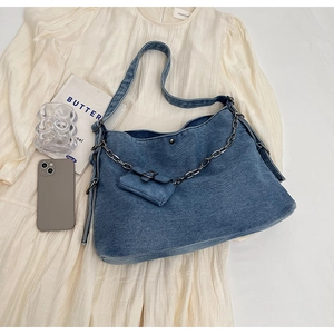 Detail of blue denim tote bag with heavy metal chain and mini pouch on fabric backdrop