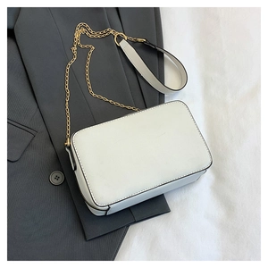 Detailed top view of a white cassette-shaped crossbody bag with gold chain on a grey blazer