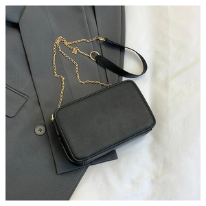 Detail of a matte black leather cassette crossbody bag with a gold chain strap on grey fabric