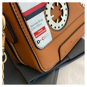 Macro view showing the detailed stitching and retro cassette print on a brown crossbody bag