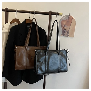 Detail minimalistischer schwarzer und brauner PU-Ledershopper an einem Holzkleiderbügel
