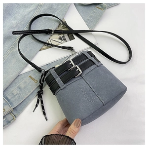Dettaglio della borsa a secchiello in denim blu con cinture in pelle nera e coulisse
