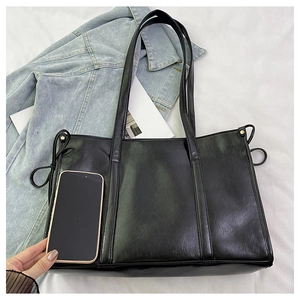 Detail-Größenvergleich einer schwarzen Shopper-Tasche aus Leder neben einem Smartphone