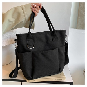 Detail view of black canvas tote bag with front pockets and adjustable wide shoulder strap
