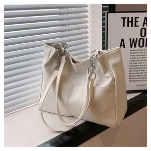 Detail of off-white faux leather tote bag with silver chain strap on window sill
