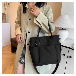 Detailed view of black canvas tote bag with front pockets on beige trench coat model