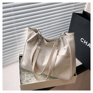 Detail of a cream faux leather tote bag with metallic chain strap in a gift box setup