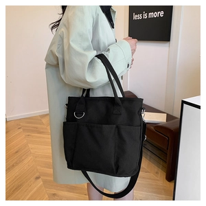 Detail of black canvas tote bag with triple front pockets and adjustable shoulder strap