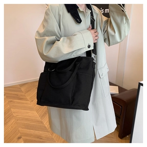 Detail of black canvas tote bag showing side pocket and adjustable nylon strap on model