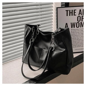 Detail shot of the black leather tote bag featuring stylish metal chain straps and stitching
