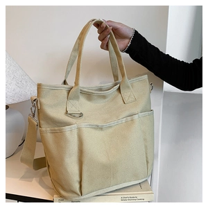 Detail view of beige canvas tote bag showing three front pockets and sturdy handles