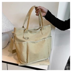 Detail view of beige canvas tote bag with functional exterior pockets and adjustable strap