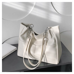 Detail view of off-white tote bag featuring silver chain straps and side pocket texture