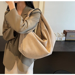 Close-up of a large beige suede tote bag with wide shoulder strap worn by a model