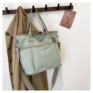 Detailed view of sage green canvas tote bag with large front pockets and crossbody strap