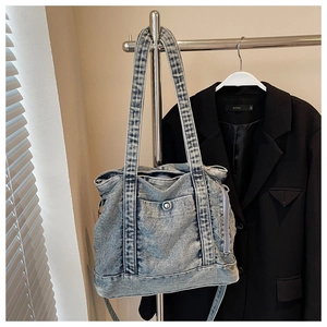 Detailed close-up of a washed blue denim tote bag showing pockets and metal buckles