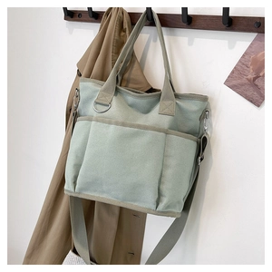 Close-up of light green canvas tote bag with triple front pockets and adjustable strap