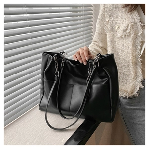 Detail of a black PU leather tote bag with silver chain straps and front pockets