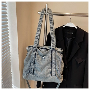 Detail of light blue washed denim tote bag with metal button pocket and zipper accents