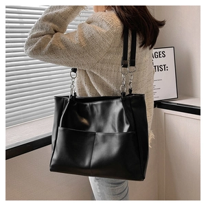 Detail of black leather tote bag featuring metal ring chain straps and outer pocket