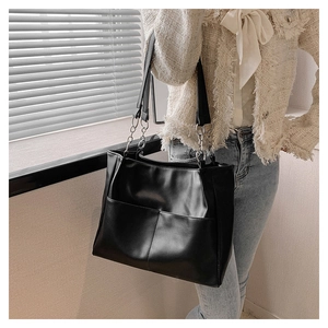 Detail of black tote bag featuring matte leather texture and silver chain handles