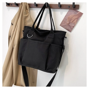 Detail shot of black canvas tote bag with front pockets and D-ring on wooden hanger
