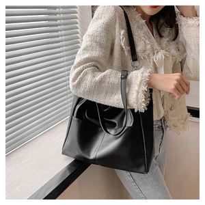 Detail of a large black matte tote bag worn with a tweed jacket and denim jeans