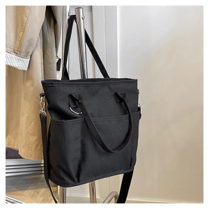 Close-up of black canvas tote bag showing multiple pockets and adjustable shoulder strap