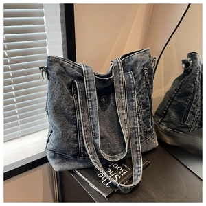 Detailed texture of washed denim tote bag with metal zippers and long shoulder strap