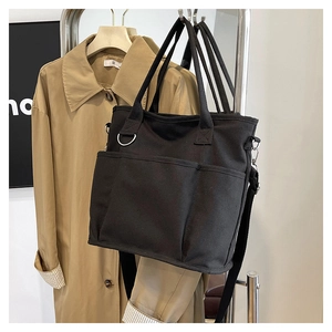 Detailed close-up of a black canvas tote bag with multi-pockets and adjustable strap